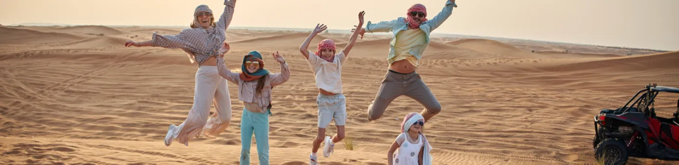 Gezin in woestijn springt vrolijk in de lucht bovenop zandduin